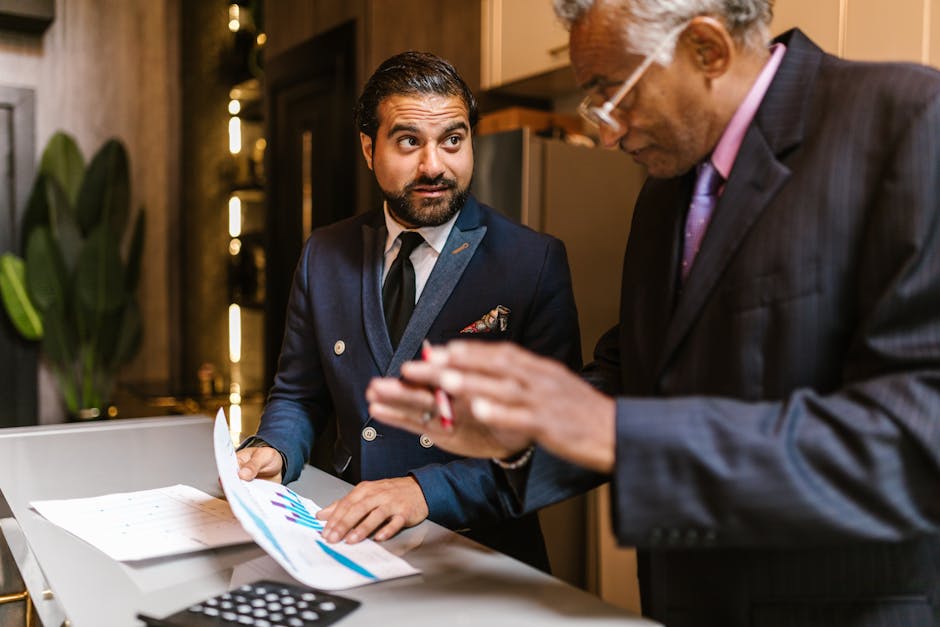 Two men in suits discuss financial documents with graphs indoors.